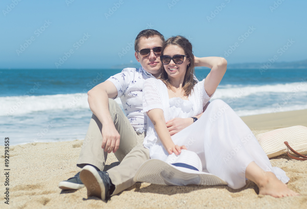 Young smiling couple in sunglasses sitting on the beach