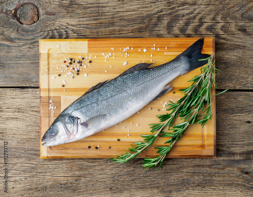 fresh, raw, saltwater fish, sea bass on a wooden cutting board on old wooden aged, rustic table, top view
