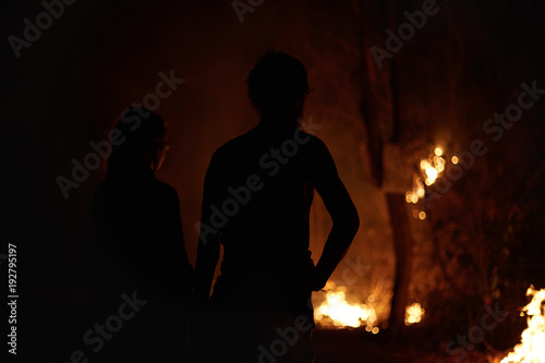 Earth is on fire. Back view of two silhouettes  of young international tourists watching as the forest burns on purpose by the Northern Thailand farmers, destroying nature for illegal ideas.