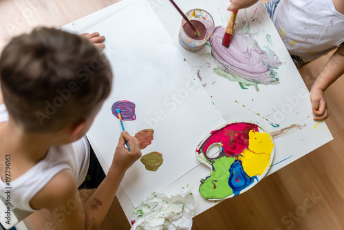 Two kids painting with water colors with brush