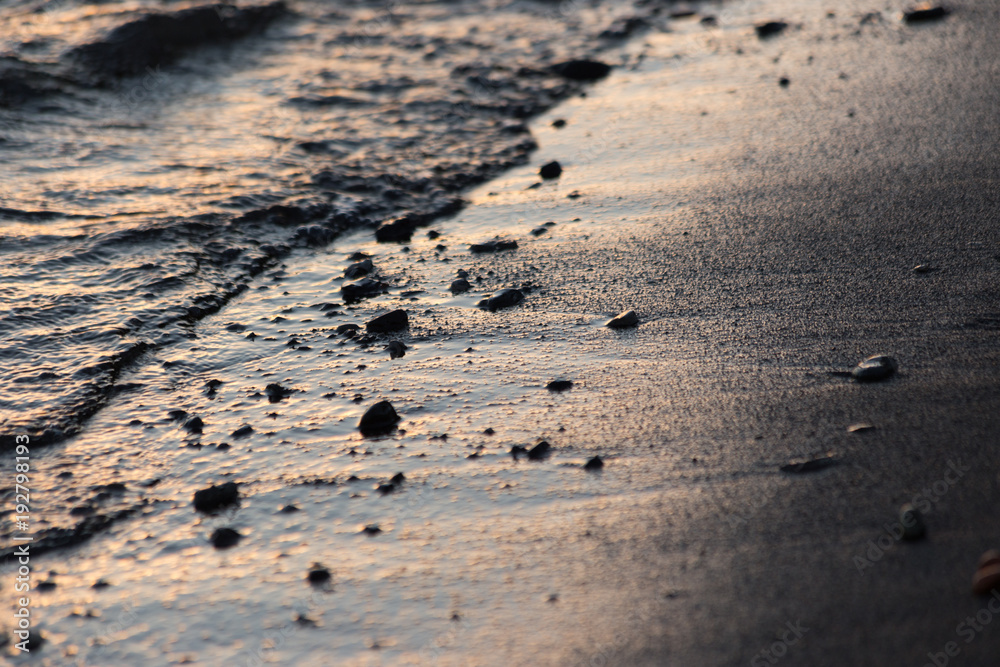 A close view of water on a lake shore at sunset, with details of sands and little round stones A close view of water on a lake shore at sunset, with details of sands and little round stones
