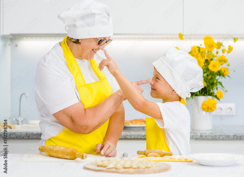 Senior woman and young boy indulge in the kitchen, trying to stain each other with flour Senior woman and young boy indulge in the kitchen, trying to stain each other with flour