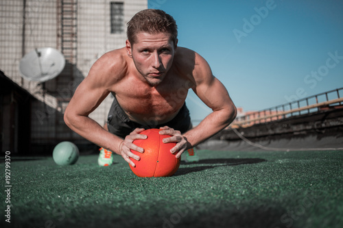 Front view of man standing in plank with hands on the ball. Sport exercises on the roof of the building. photo