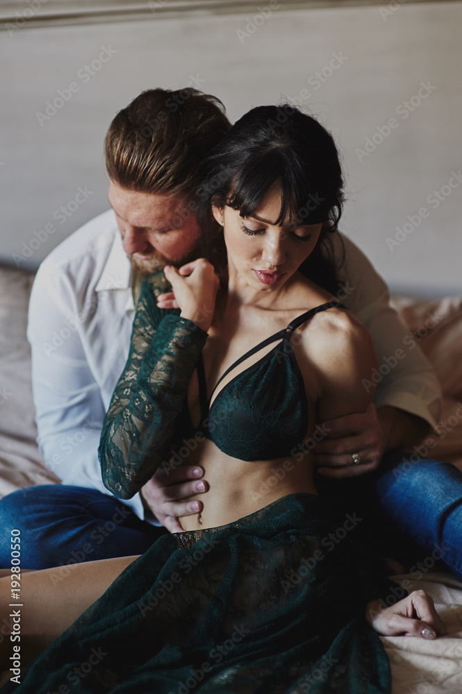 Strong Man and beautiful woman lying on the bed intimate atmosphere. Luxurious furniture and beautiful interior. A girl with black hair is a man without a shirt. Love and tenderness.