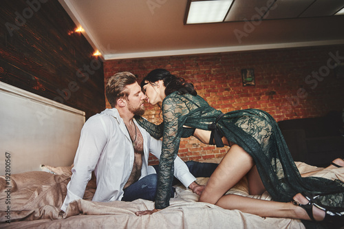 Strong Man and beautiful woman lying on the bed intimate atmosphere. Luxurious furniture and beautiful interior. A girl with black hair is a man without a shirt. Love and tenderness.