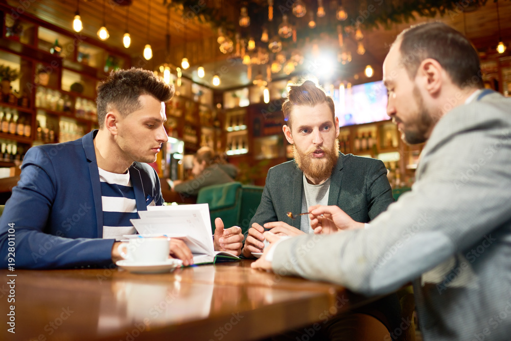 Working meeting in spacious cafe: group of hard-working colleagues brainstorming on ambitious project while sitting at table