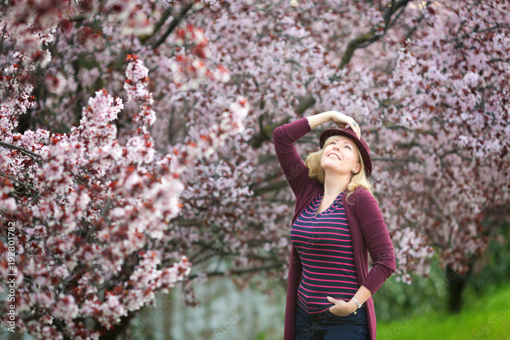 Caucasian blond woman with long hair in purple fedora hat near blossoming tree Caucasian blond woman with long hair in purple fedora hat near blossoming tree