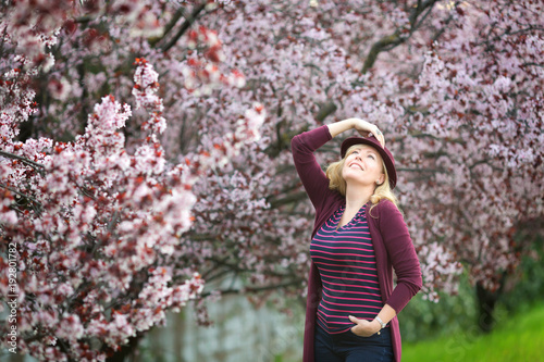 Caucasian blond woman with long hair in purple fedora hat near blossoming tree