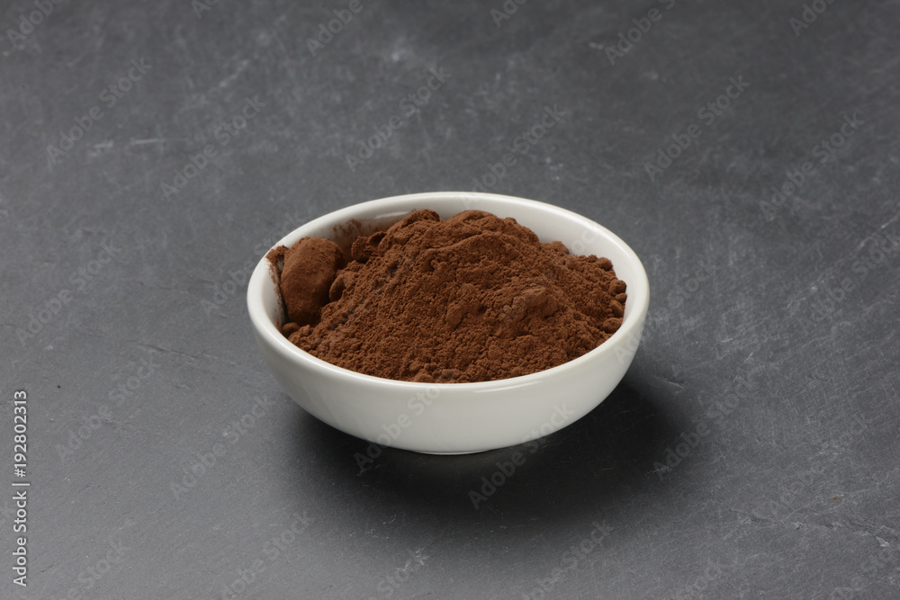 Cacao en polvo en un bol de cerámica blanco sobre un fondo de piedra negra Cacao en polvo en un bol de cerámica blanco sobre un fondo de piedra negra