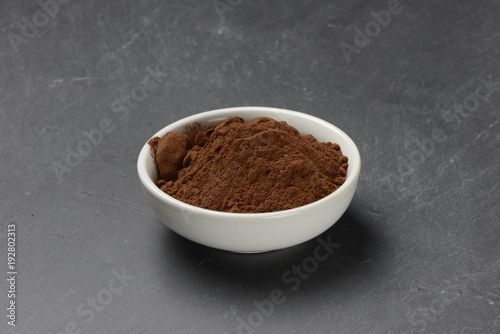 Cacao en polvo en un bol de cerámica blanco sobre un fondo de piedra negra