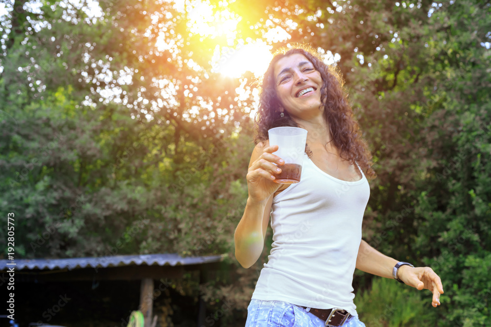 Happy young woman drinking cold drink and having fun outside at forest. Summer concept