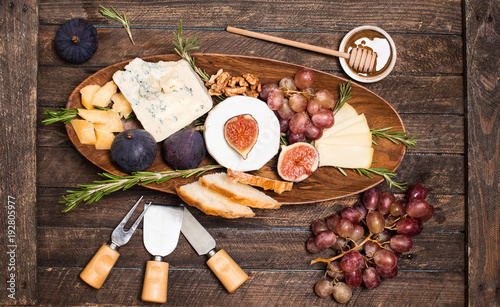 Cheese board. Various types of cheese. Cheese plate with cheeses Parmesan, Brie, Camembert and Roquefort serving with grapes, honey, nuts, olives and bread on wooden board.