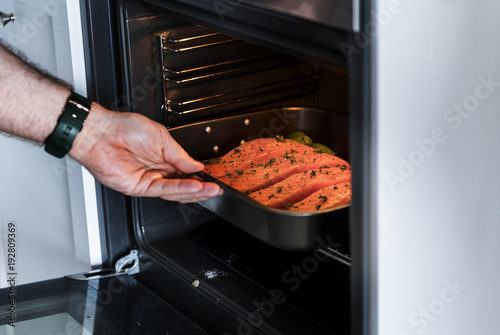 Man putting raw salmon steak into oven photo