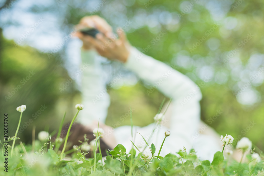 Obraz premium 公園の芝生でスマホを使う女性