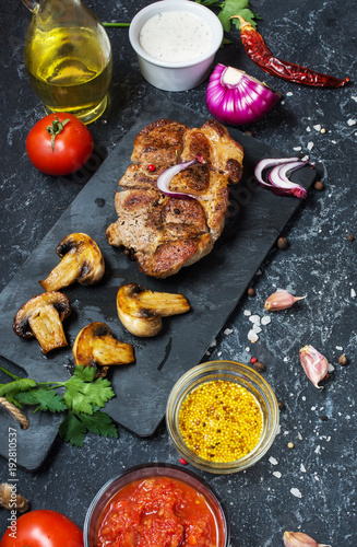 Juicy pork steak with spices and grilled mushroomson dark stone background