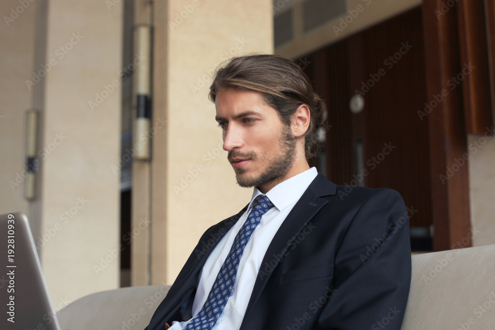 Young businessman working on laptop, sitting in hotel lobby waiting for someone. Young businessman working on laptop, sitting in hotel lobby waiting for someone.