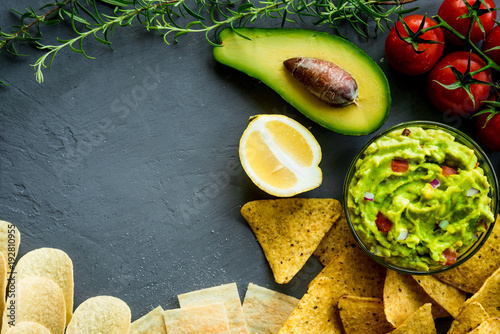 Guacamole bowl with ingredients and tortilla different tipes of chips on a stone table. Top view image. Copyspace for your text. photo