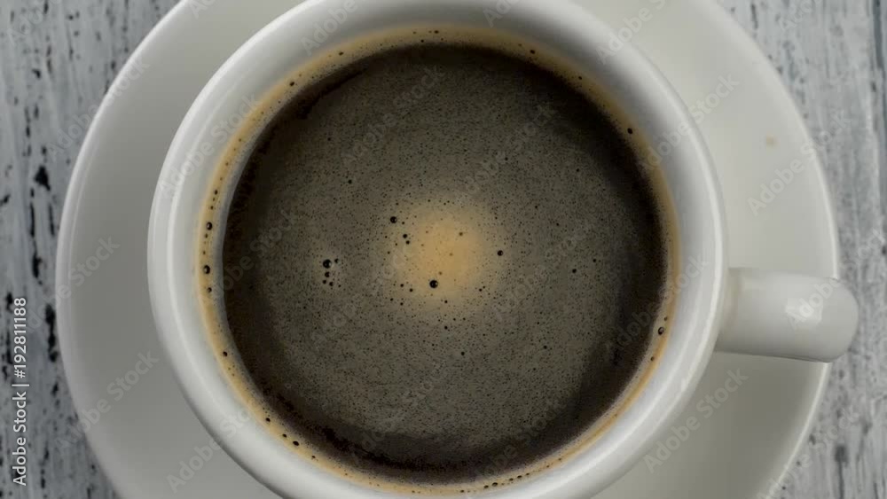 Coffee foam swirls in white cup with coffee. Shabby white wooden background. Top down view.
