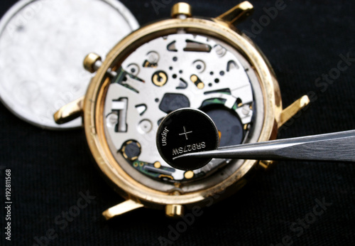 watchmaker change battery, close up of battery and quartz watch caliber in the background