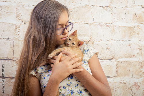 Girl with a favorite kitten. Young girl is holding a red kitten. cute kitten. Little red cat on the hands of girl. beige brick background. Home pets. Tenderness and Love 