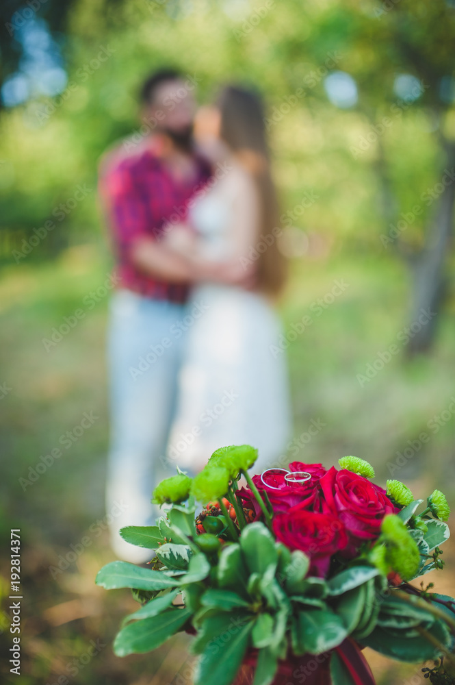In the foreground a wedding bouquet of flowers, in the background, blurry girl and a guy are standing. Embrace in the background. In the foreground a wedding bouquet of flowers, in the background, blurry girl and a guy are standing. Embrace in the background.