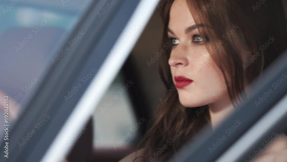 Young woman with aggressive face expression is inside a car. She is on a driver seat, holding wheel, door is open, camera is outside, close-up Young woman with aggressive face expression is inside a car. She is on a driver seat, holding wheel, door is open, camera is outside, close-up