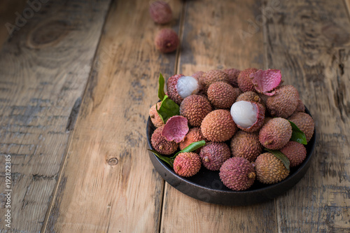 Still life of fresh lychee fruits in a black plate on a wooden background. Rustic style