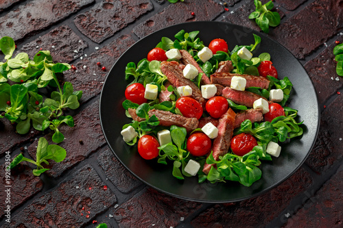 Juicy Beef Sirloin Steak Salad with roasted tomatoes, feta cheese and green vegetables in a black plate. healthy food