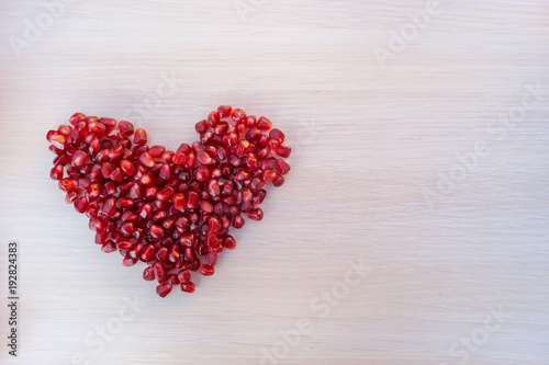 Heart made from grains of garnet on wooden table. Space for text