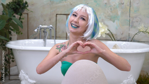 Beautiful woman in wig making heart symbol with her hands in bathroom