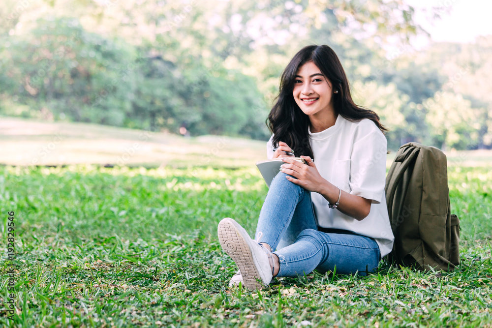 Woman relaxing with pen writing on a notebook sitting on grass in park Woman relaxing with pen writing on a notebook sitting on grass in park
