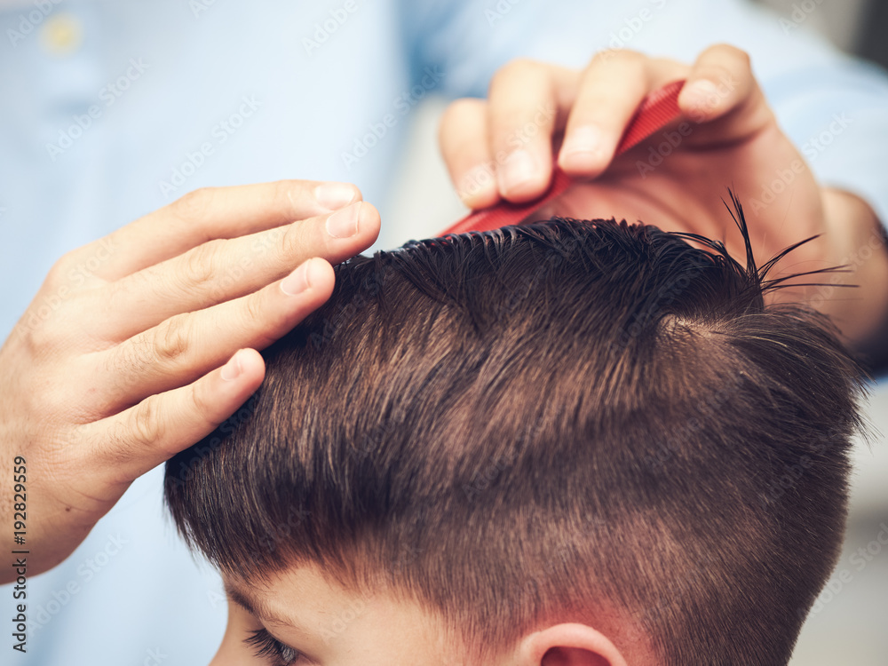 Naklejka premium Barber is making haircut to boy in barbershop. Close view.