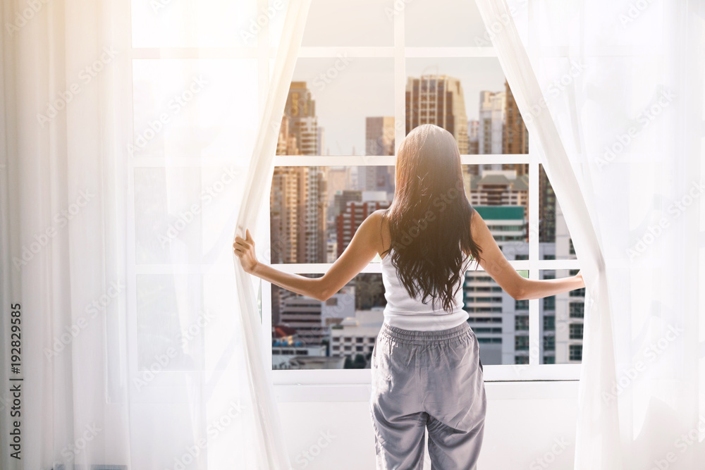 Woman waking up and opening window curtains at home Woman waking up and opening window curtains at home