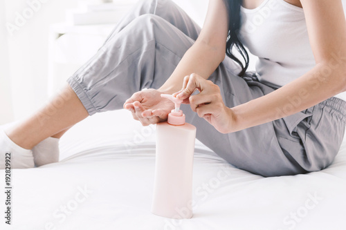 Woman applying cream on hand on bed
