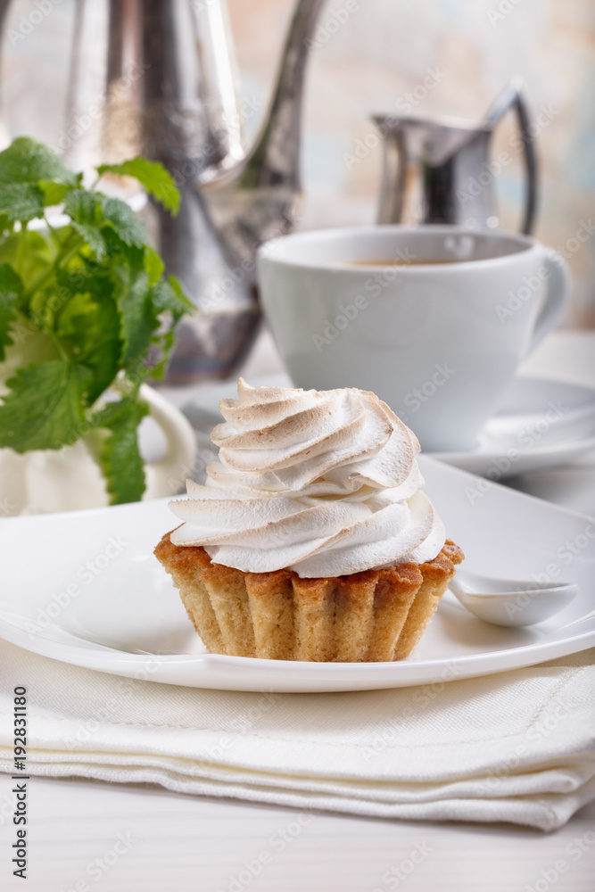 Delicious tartlets with meringue on top. Coffee and cupcakes served on white table. Delicious tartlets with meringue on top. Coffee and cupcakes served on white table.