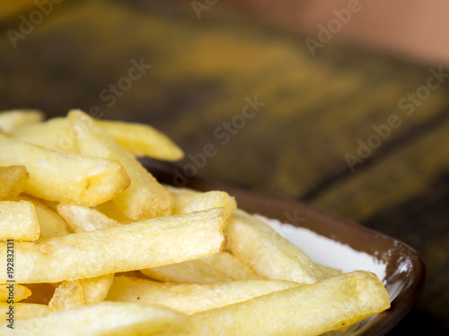 fried French fries on a white plate with brown border on the wooden table