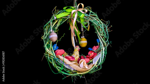 Easter wreath on a black background, braided from a vine, with colorful ribbons and hanging eggs