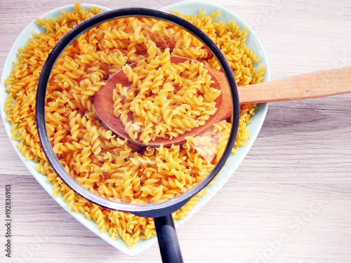 a bowl of pasta on a wooden floor,a wooden spoon and magnifying glass.food,