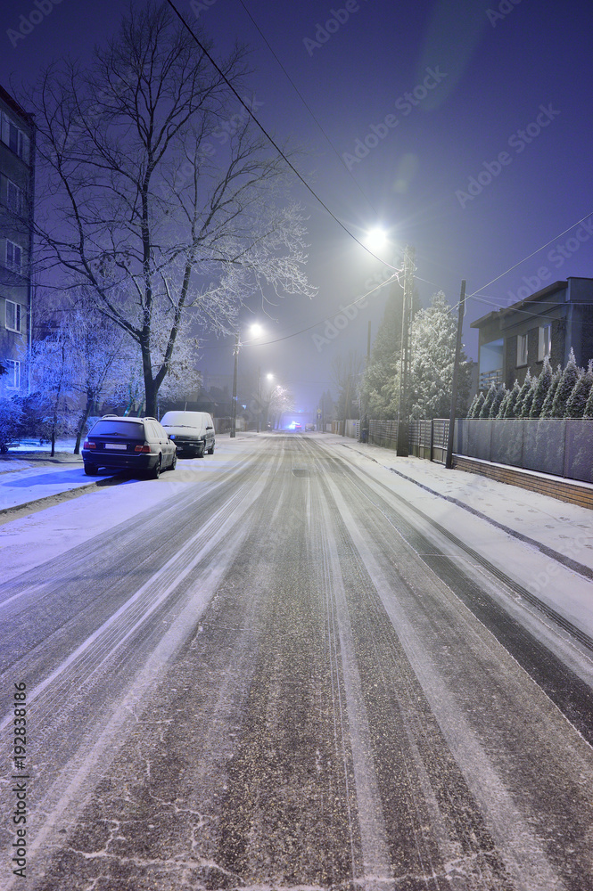 Ulica w zimową noc pokryta sniegiem i ślady samochodów.