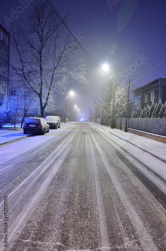 Ulica w zimową noc pokryta sniegiem i ślady samochodów.
