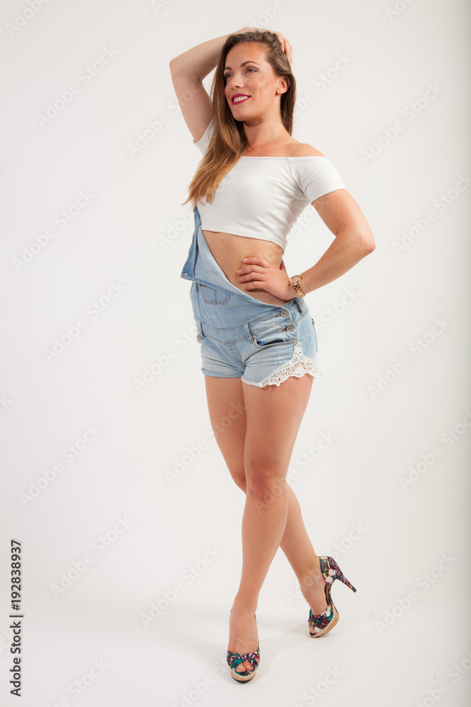 portrait of a young lady in standard up right fashion pose, wearing a white top, blue jeans dungarees and high heels portrait of a young lady in standard up right fashion pose, wearing a white top, blue jeans dungarees and high heels