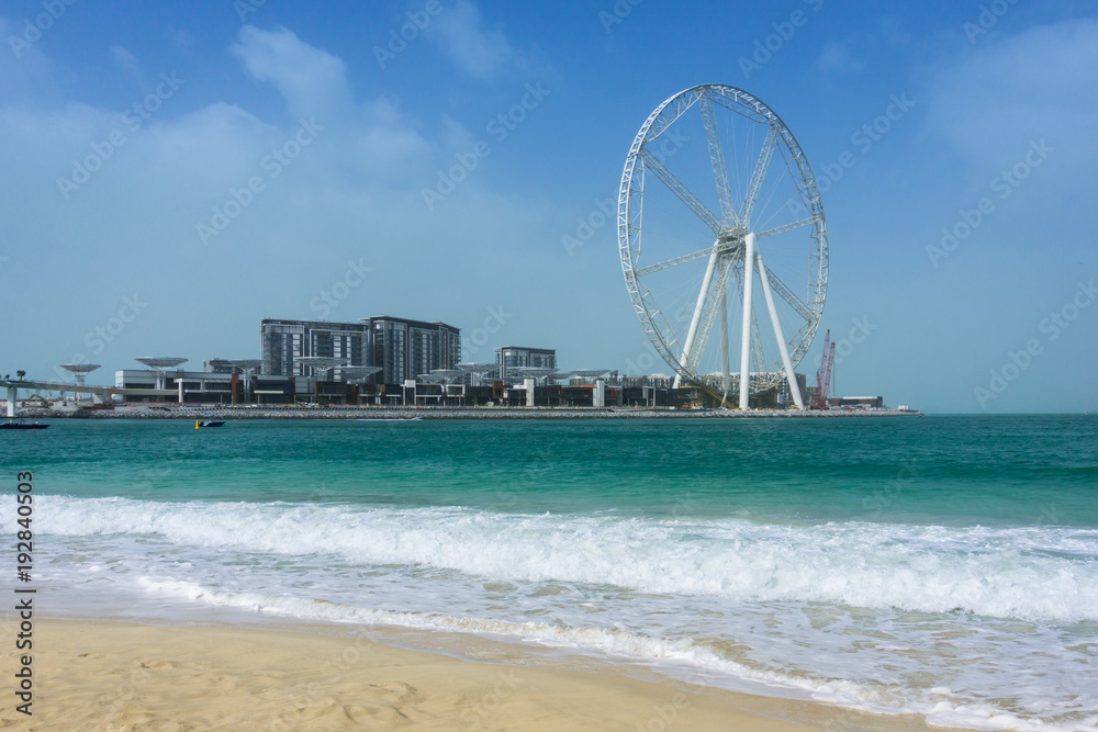 The Ain Dubai ferris wheel under construction, daytime, view from the coast of JBR Beach to the Bluewater Island. Dubai, UAE.