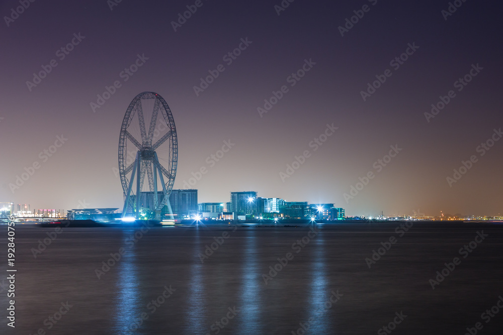 The Ain Dubai ferris wheel under construction, night cityscape with illumination, Bluewater Island, Dubai, UAE.