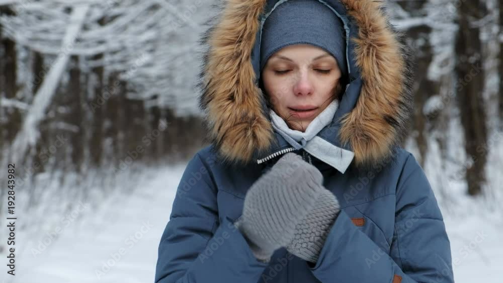Close-up woman warms her hands in the cold with her breath in winter forest. Close-up woman warms her hands in the cold with her breath in winter forest.