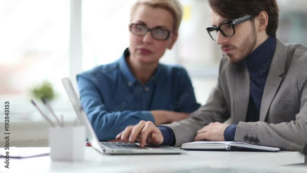 Cinemagraph of stylish male manager pressing button on laptop keyboard while sitting at office table with female colleague Cinemagraph of stylish male manager pressing button on laptop keyboard while sitting at office table with female colleague