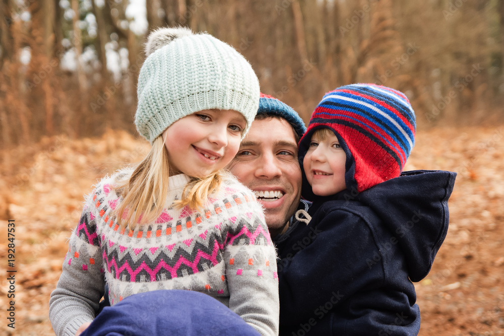 father hugging son and daughter outside at park during wintertime father hugging son and daughter outside at park during wintertime