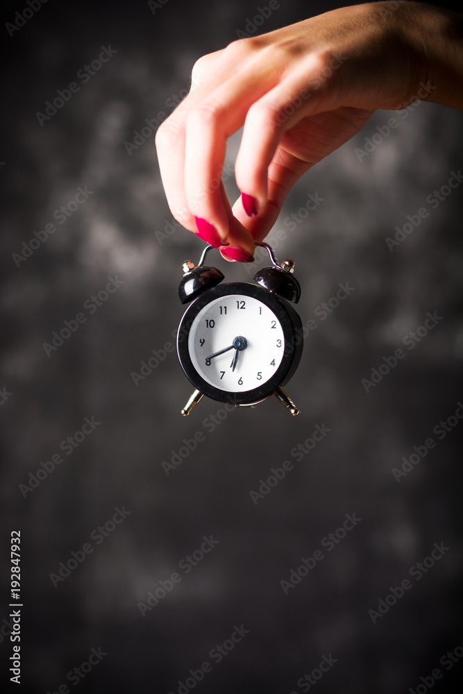 Female hand holding a small clock Female hand holding a small clock