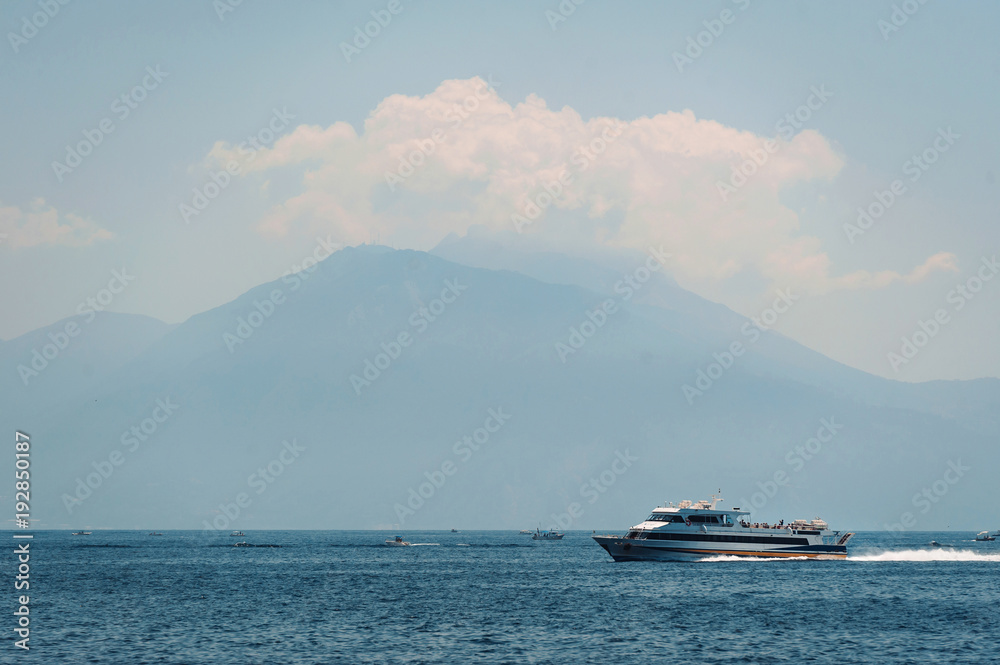 Ferry moves across the blue Mediterranean sea. Foggy mountains background. Mountains in the distance.