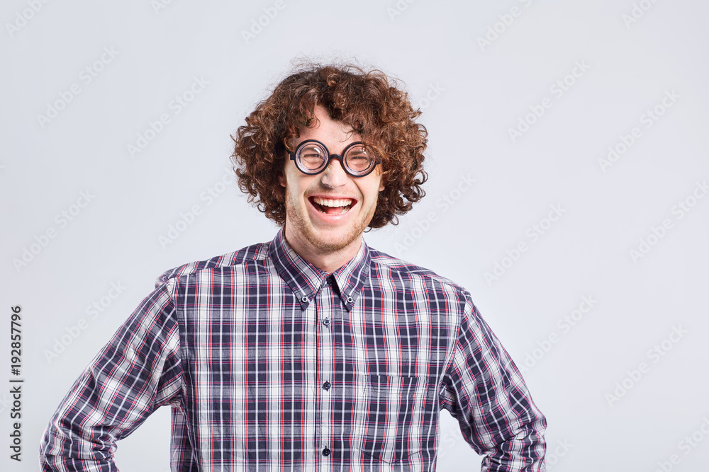 Curly nerd man in glasses with a stupid kind of funny emotion on a gray background.