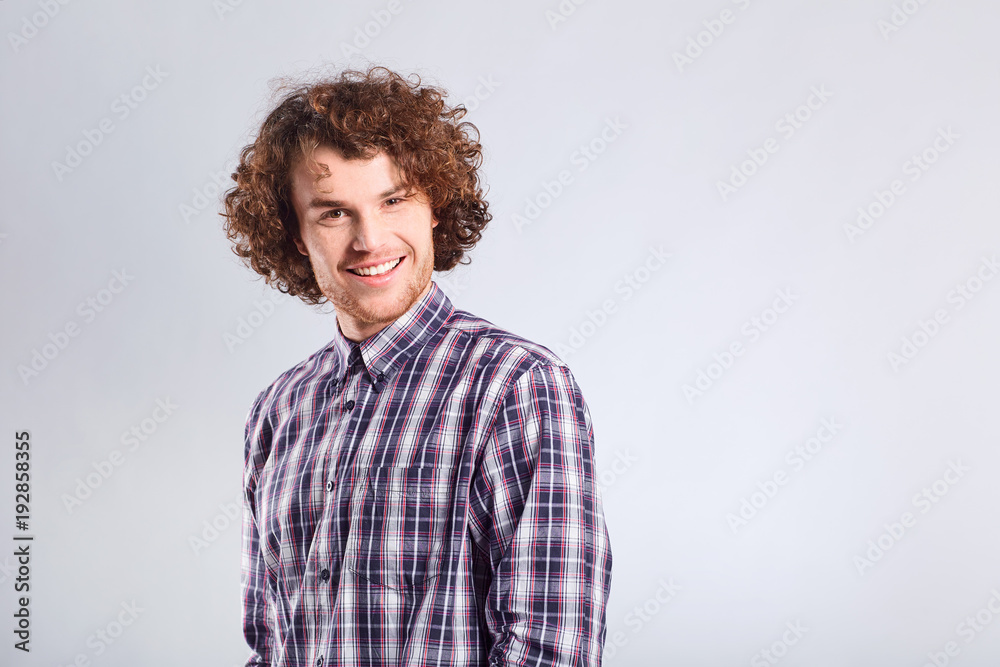 Curly guy smiles with a positive emotion up against a gray background. Curly guy smiles with a positive emotion up against a gray background.